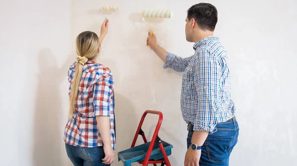 Feliz familia joven pintando paredes con rodillos de pintura — Foto de Stock