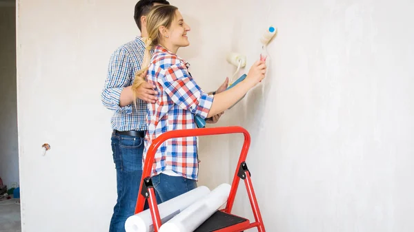 Retrato de pareja joven pintando paredes en casa nueva con pintura blanca —  Fotos de Stock