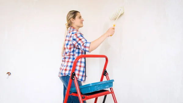 Hermosa joven sonriente con rodillo de pintura haciendo renovación en casa — Foto de Stock