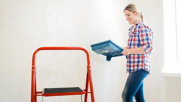 Hermosa mujer sonriente sosteniendo la cubeta de pintura y paredes de pintura — Foto de Stock