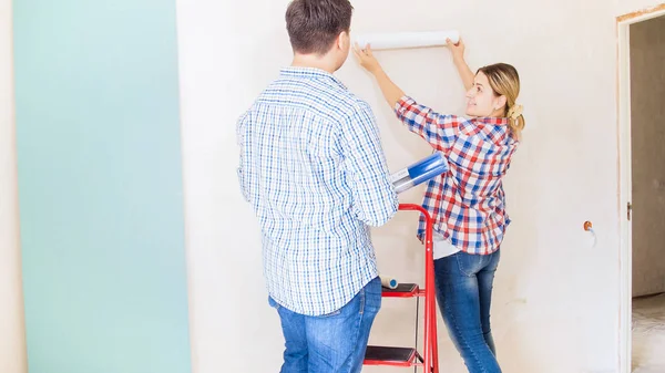 Junge Frau mit Ehemann schaut sich Tapetenfarbe in neuem Haus an — Stockfoto