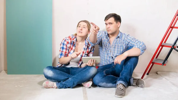 Jeune couple assis dans la maison en rénovation et en choisissant des lieux pour de nouveaux meubles — Photo