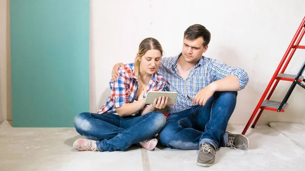 Familia joven eligiendo muebles en tableta digital para su nuevo hogar —  Fotos de Stock