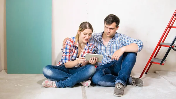 Молода пара сидить на підлозі свого нового будинку і використовує цифровий планшет — стокове фото