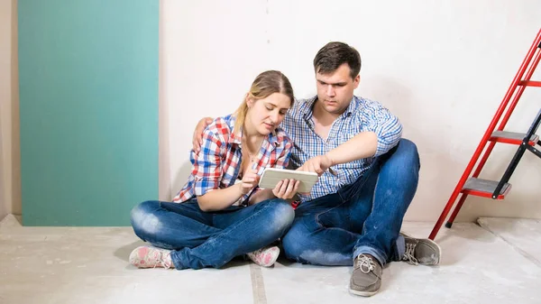 Молодая пара сидит на полу в доме под строительство и с помощью цифрового планшетного компьютера — стоковое фото