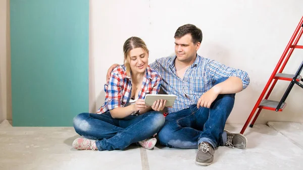 Usmíval se mladý pár s digitálním tabletu sedí na patře nového domu probíhá rekonstrukce — Stock fotografie