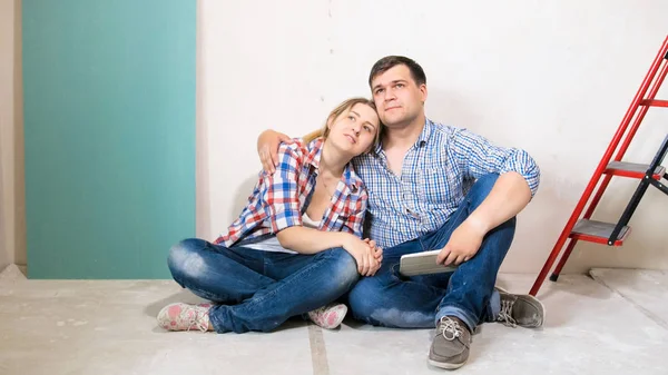 Pareja joven sentada en el suelo de la manguera en construcción y soñando con un nuevo hogar —  Fotos de Stock