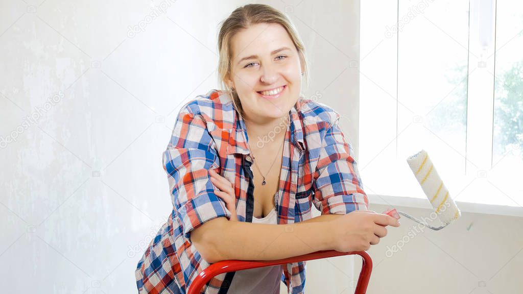 Beautiufl young woman in checkered shirt with paint roller looking in camera