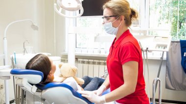 Daha önce tedavi diş dişçi sandalyede oturan bir oyuncak ayı ile şirin kız