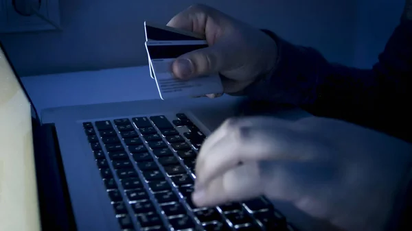 Closeup image of young man holding credit cards and working on laptop at night. Concept of e-shopping or e-commerce — Stock Photo, Image