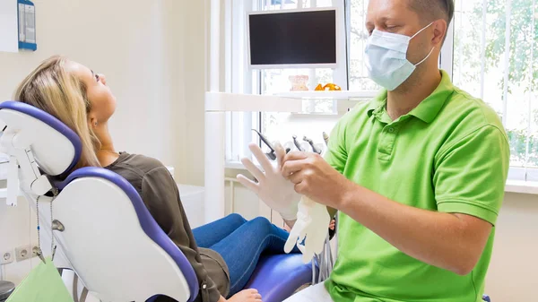 Retrato do dentista masculino sentado no escritório e usando luvas de látex — Fotografia de Stock