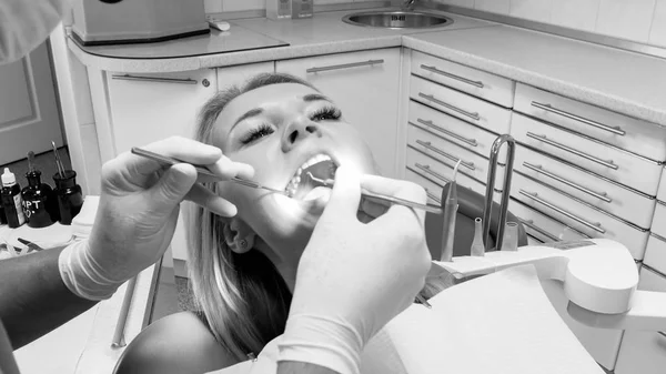 Zwart-wit beeld van tandarts inspecing dames tanden met spiegel — Stockfoto