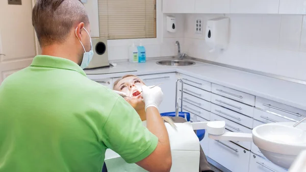 Citra tampilan belakang dari dokter gigi memeriksa pasien rongga mulut dengan instrumen khusus — Stok Foto