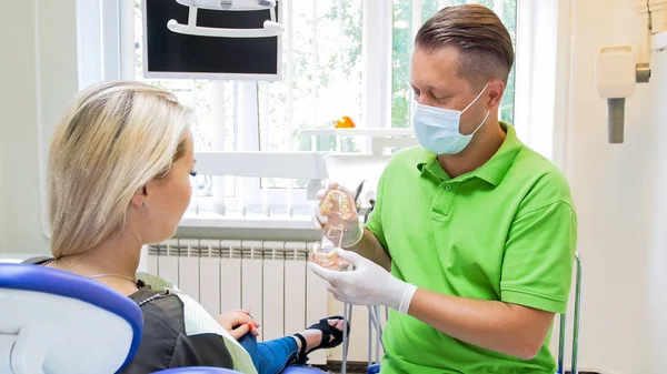 Dentista masculino usando modelo de mandíbula de plástico para explicar o tratamento para seu paciente — Fotografia de Stock
