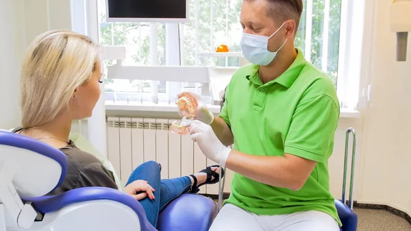 Porträtt av manliga tandläkare visar plast tänder modell till sin patient — Stockfoto