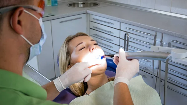 Jovem loira sentada na cadeira do dentista enquanto seus dentes estão sendo tratados por fotopolímero e lâmpada UV — Fotografia de Stock
