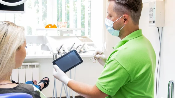 Porträtt av manliga tandläkare hålla digital tablett och visar det att hans patient. Plats för din text eller bild på skärmen — Stockfoto
