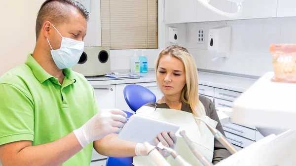 Portrait of young woman listening to her dentist and looking at digital tablet scrren — Stock Photo, Image