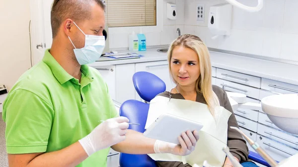 Portrait of dentist holding digital tablet and showing it to his patient — Stock Photo, Image