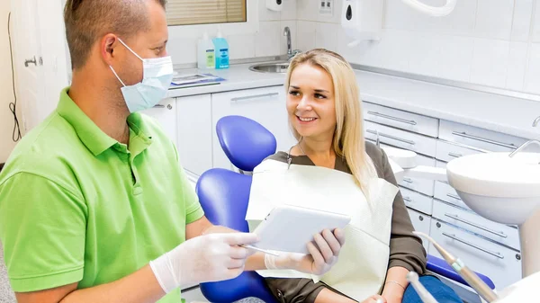 Retrato de bela mulher sorridente sentada no consultório odontológico e conversando com o dentista — Fotografia de Stock