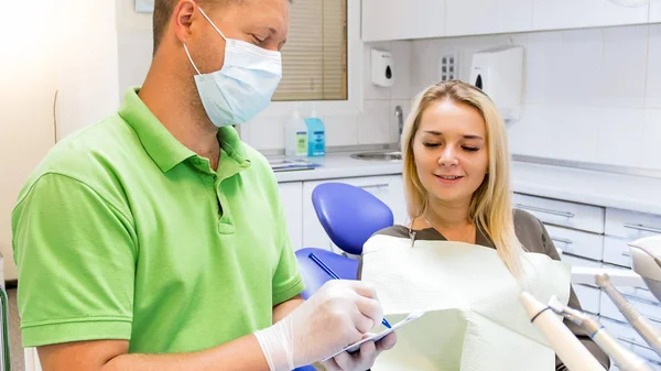 Mulher bonita sentada na cadeira do dentista e olhando como médico escreve prescrição — Fotografia de Stock