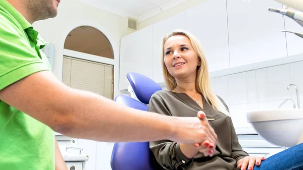 Közelkép kép fogorvos kezet rázott a mosolygó fiatal nő ül a fogorvos szék — Stock Fotó