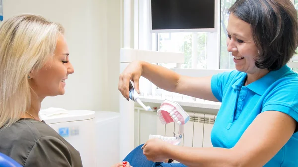 Mosolyogva női fogorvos tanítás ő beteg használata az elektromos fogkefe — Stock Fotó