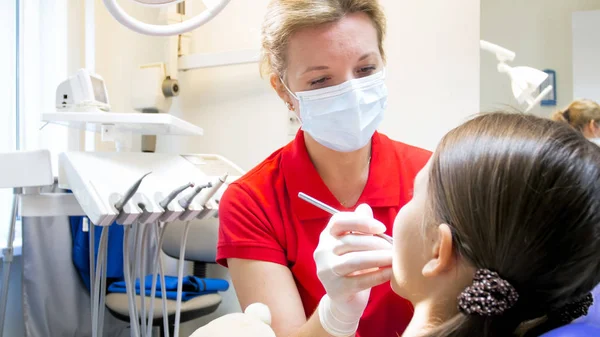 Портрет стоматолога, осматривающего зубы маленьких девочек в клинике — стоковое фото