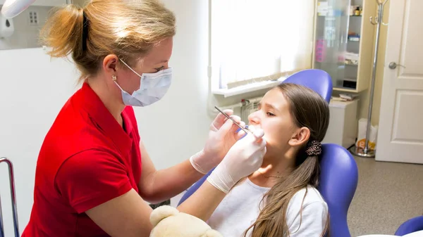 Dentista pediátrico feminino inspecionando dentes meninas com instrumentos — Fotografia de Stock