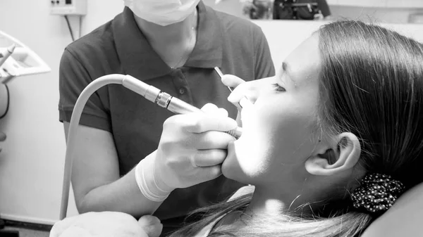 Zwart-wit portret van meisje zit in de tandarts stoel terwijl haar tanden wordt terug — Stockfoto