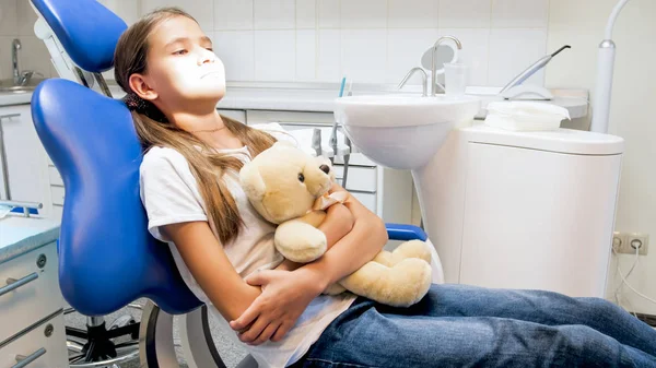 Little girl sitting in dentist chair with toy teddy bear in clinic — Stock Photo, Image