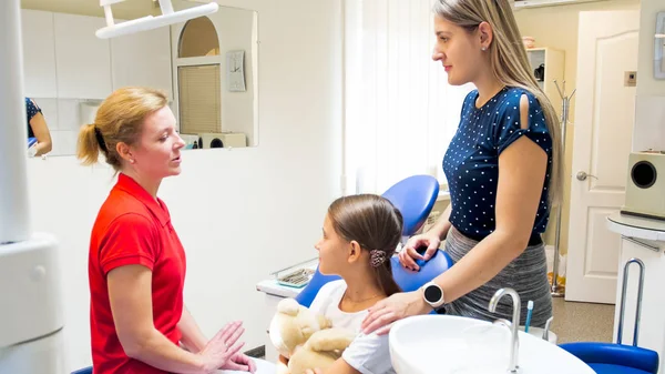 Dentista pediátrica feminina conversando com menina e sua mãe no consultório odontológico — Fotografia de Stock