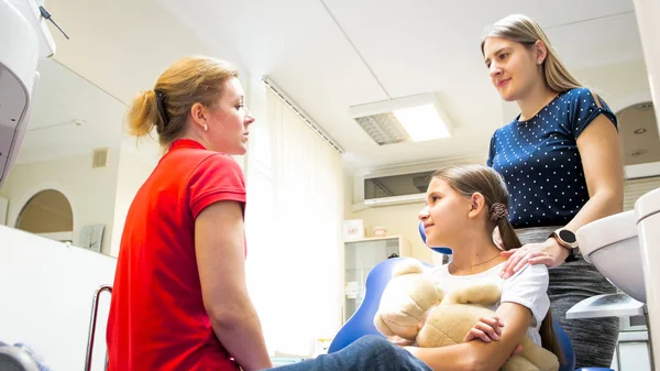 Jovem mãe com a filha conversando com o dentista pediátrico — Fotografia de Stock