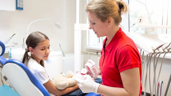 Jovem dentista pediátrica mostrando modelo de dentes para seu paciente — Fotografia de Stock