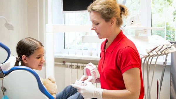 Menina sentada na cadeira do dentista e ouvindo sobre higiene dos dentes — Fotografia de Stock