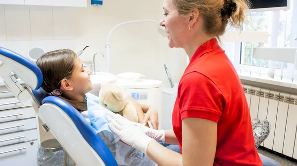 Sorrindo dentista pediátrico falando com menina bonito sentado na cadeira do dentista — Fotografia de Stock