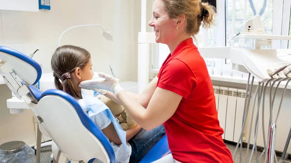 Uśmiechający się pediatric dentysta ogląda jej pacjent siedzi w fotelu u dentysty — Zdjęcie stockowe