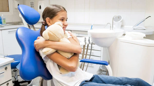 Retrato de niña feliz sonriente abrazando oso de peluche en la oficina del dentista — Foto de Stock