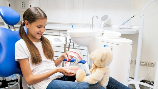 Menina bonito explicando ao ursinho de pelúcia como limpar adequadamente os dentes — Fotografia de Stock