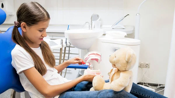 Tonårig flicka visar hennes Nalle hur man ordentligt rena tänder — Stockfoto