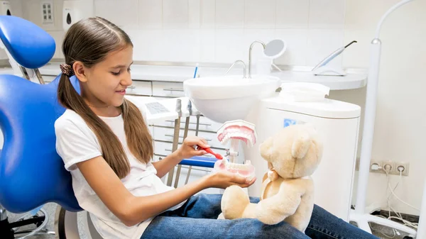 Retrato de menina sorridente ensinando seus dentes ursinhos de pelúcia limpeza no consultório odontológico — Fotografia de Stock