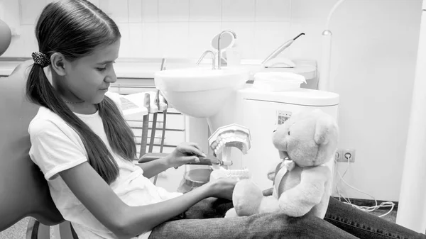 Black and white image of teenage girl teaching her teddy bear how to properly clean teeth — Stock Photo, Image