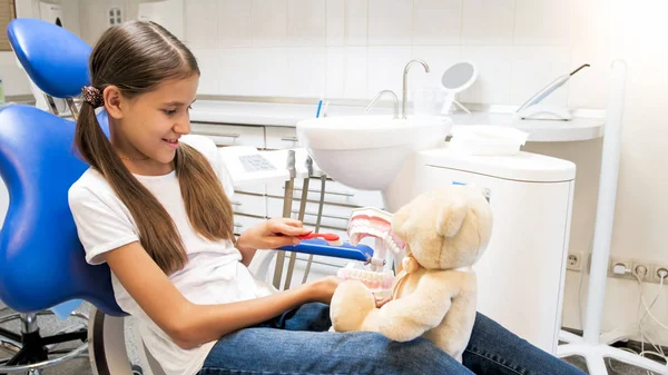 Menina sorridente bonito jogando no dentista e paciente com seu ursinho de pelúcia — Fotografia de Stock