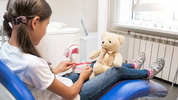 Liten flicka sitter i tandläkare stol med Björn och lära att rena tänder — Stockfoto