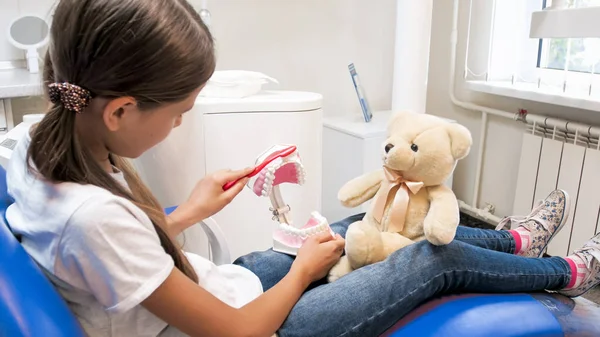 Retrato de una niña educando a su osito de peluche sobre la higiene dental en el consultorio del dentista — Foto de Stock