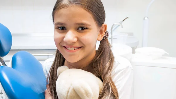 Närbild porträtt av söt leende flicka med Nalle sitter i tandläkare stol — Stockfoto