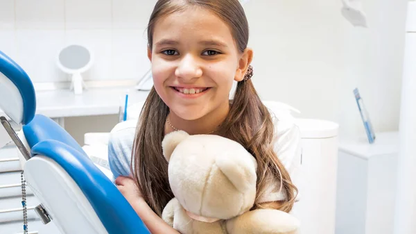 Retrato de menina sorridente feliz posando no escritório do dentista com ursinho de pelúcia — Fotografia de Stock