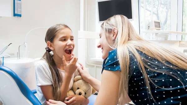 Porträtt av söt flicka visar tänder till sin mor i tandläkare kontor — Stockfoto
