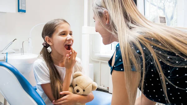 Porträtt av lilla flicka visar tänder till sin mor efter tänder behandling hos tandläkare kontor — Stockfoto