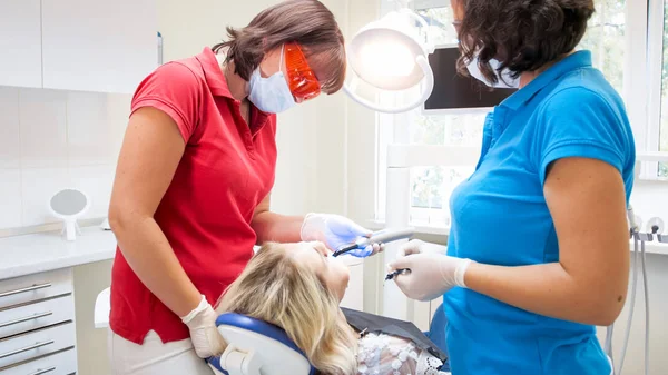 Помічник жінки, яка допомагає стоматологу в лікуванні зубів і утримує спеціальну ультрафіолетову лампу — стокове фото